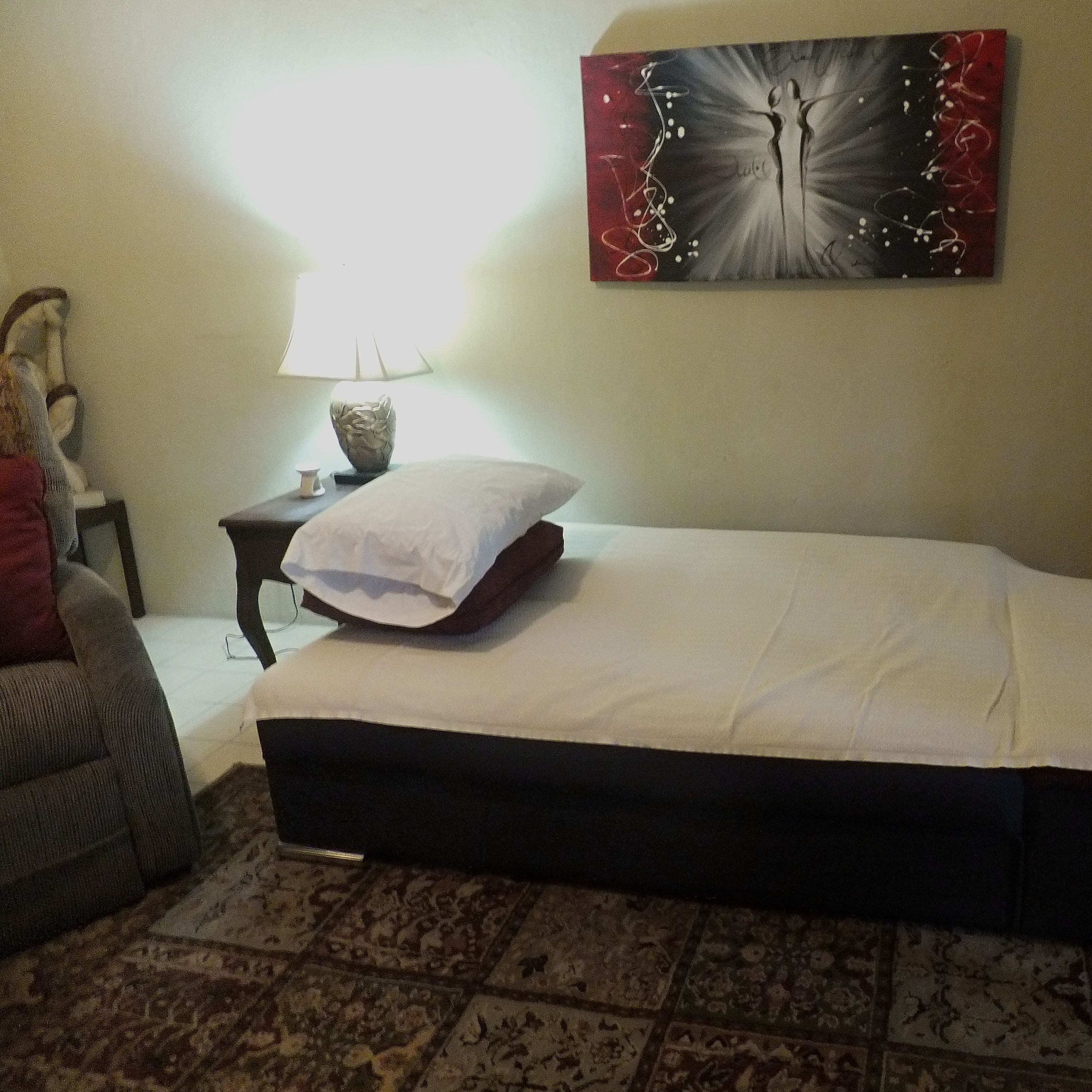 Un dormitorio con una cama, una mesita de noche, una lámpara y un adorno en la pared.