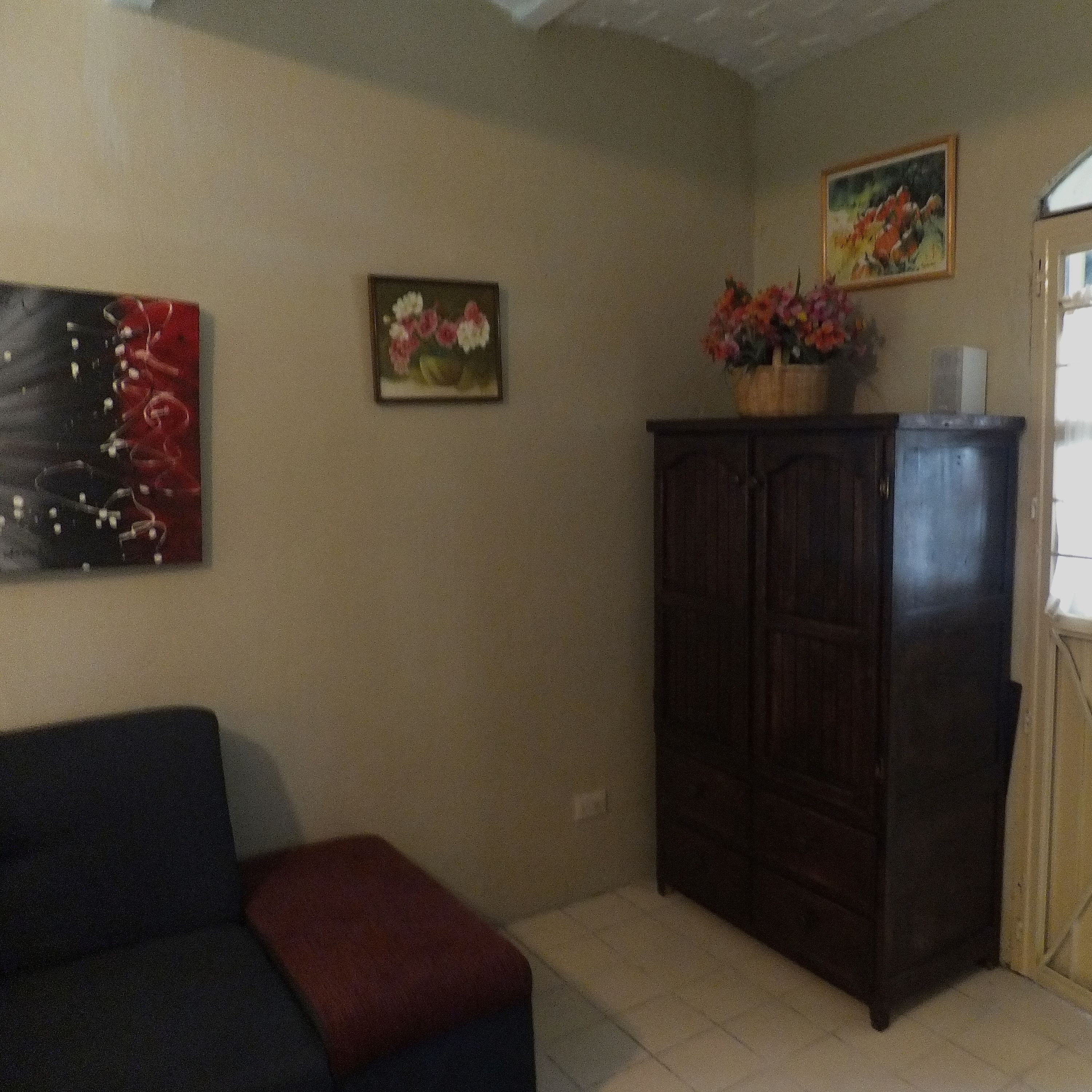A living room with a dark-colored sofa, a small red ottoman, a dark wooden cabinet, and a painting on the wall.