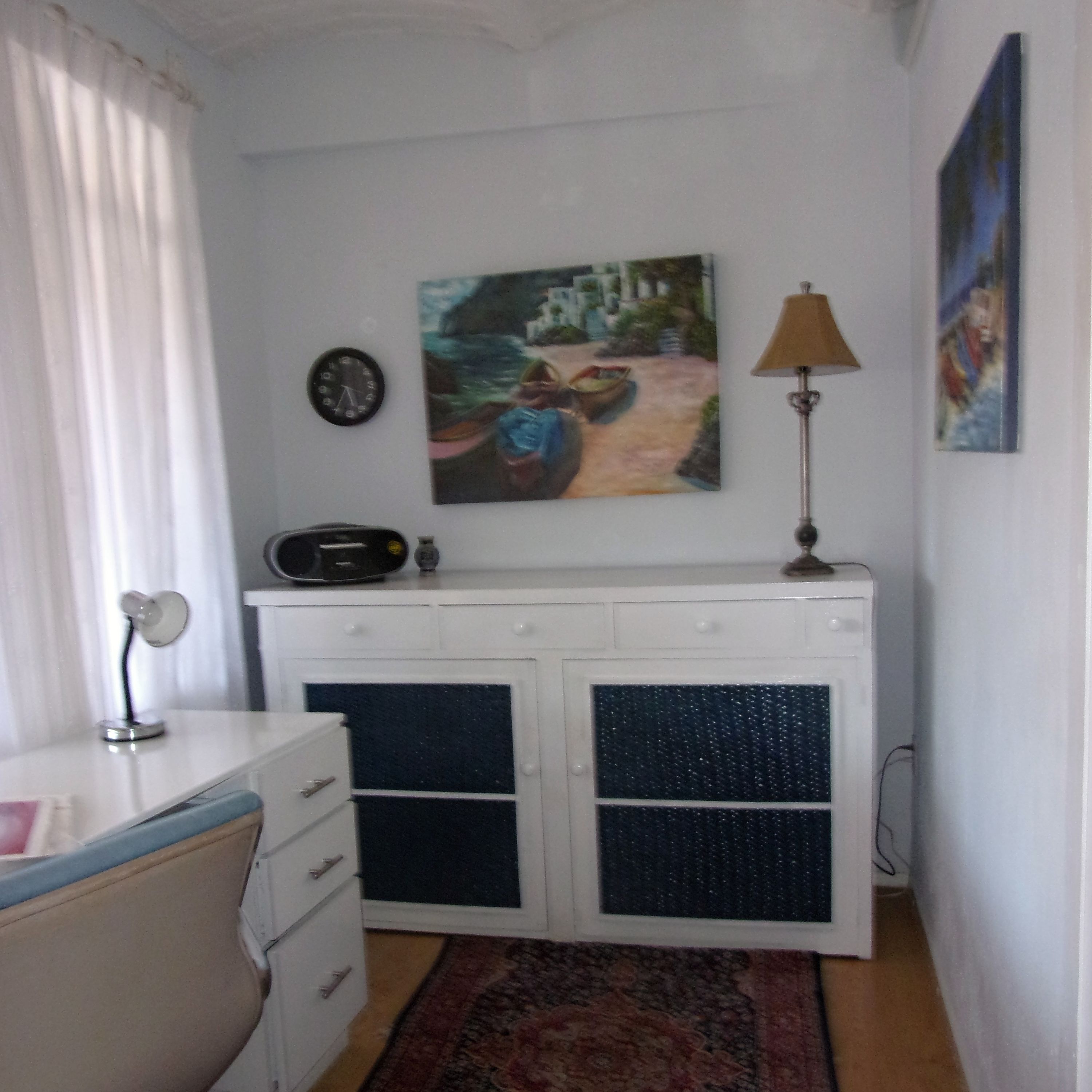 Ein Zimmer mit weißem Schminktisch, einer Uhr, einem Gemälde, einer Lampe und einem Teppich.