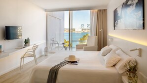A modern hotel room with a large bed, a TV, a balcony with a view of the sea, and a dining area. - Els Pins Resort and Spa (Sant Josep de sa Talaia)