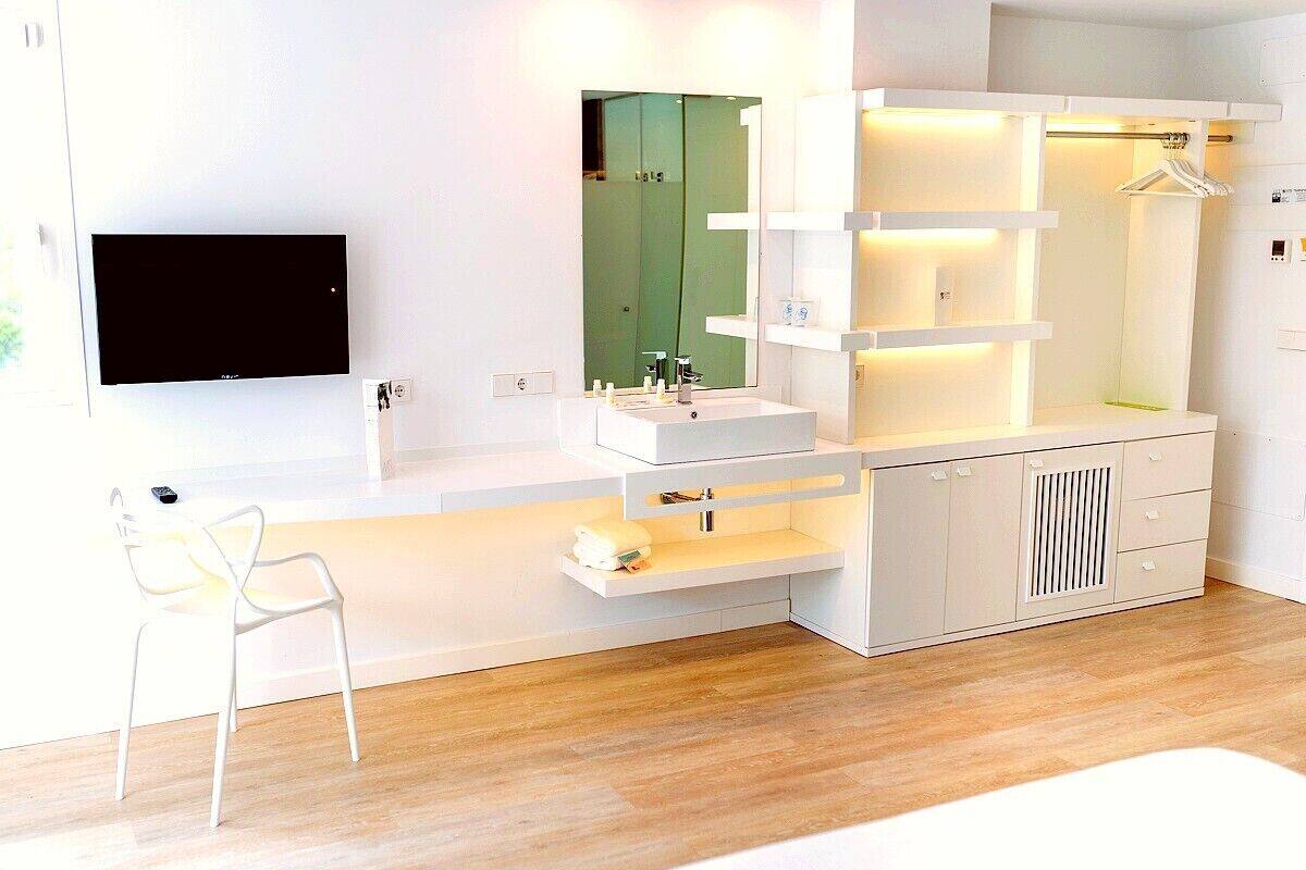 Un baño moderno con un espejo grande, muebles blancos y un televisor de pantalla plana montado en la pared.