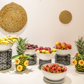 A fruit display with various types of fruits in bowls, surrounded by decorative woven baskets and a pineapple with flowers. - Els Pins Resort and Spa (Sant Josep de sa Talaia)