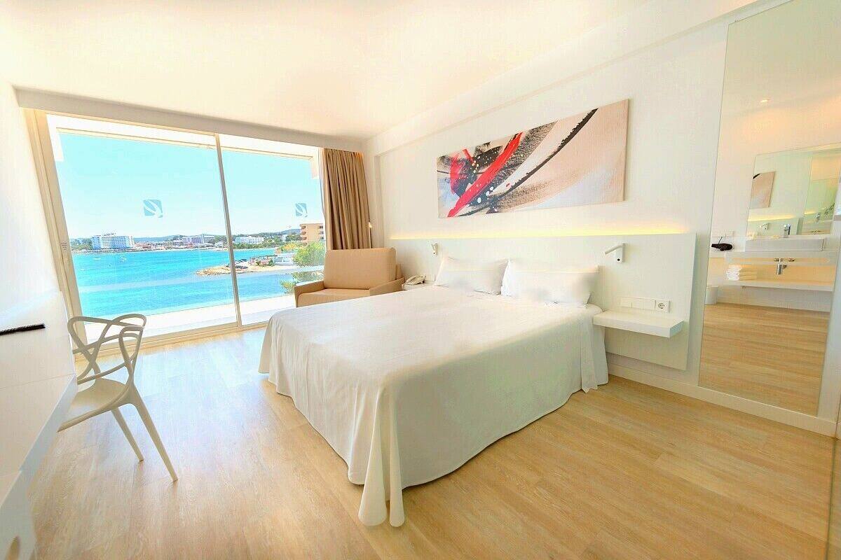 Una habitación de hotel moderna con una cama grande, una silla, un escritorio y vistas al mar.