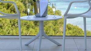 A table with two chairs, a bottle of champagne, and two glasses on a balcony overlooking a coastal landscape. - Els Pins Resort and Spa (Sant Josep de sa Talaia)