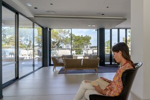 A modern interior with large windows, wicker furniture, and a person reading a book. - Els Pins Resort and Spa (Sant Josep de sa Talaia)