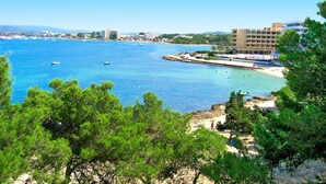 A coastal view with clear blue water, a sandy beach, and a hotel with multiple floors and balconies overlooking the sea. - Els Pins Resort and Spa (Sant Josep de sa Talaia)