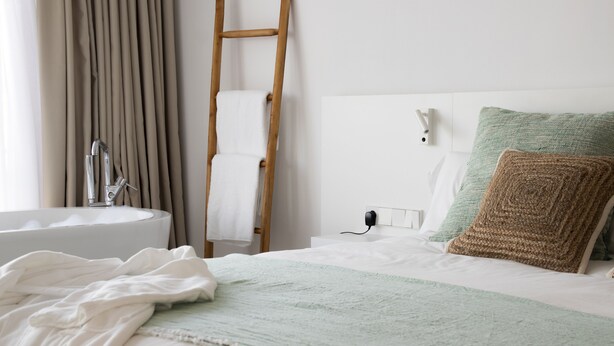 Une chambre à coucher avec un lit, une table de chevet, une lampe, une prise électrique et une fenêtre avec des rideaux.