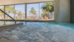 An indoor swimming pool with a view of the outdoors through large windows. - Els Pins Resort and Spa (Sant Josep de sa Talaia)