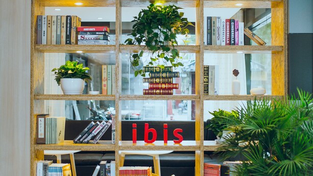 Une bibliothèque remplie de livres et de plantes, une chaise rouge et le mot « ibis » écrit sur l’étagère.