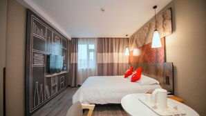 Une chambre d’hôtel avec un grand lit, un téléviseur posé sur un meuble, une petite table avec une tasse et une soucoupe, et un mur orné d’un motif géométrique.
