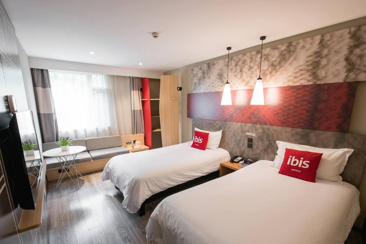 Une chambre d’hôtel avec deux lits, un canapé, une petite table et un bureau.