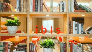 Une bibliothèque remplie de livres et ornée de deux plantes en pot, avec le mot « ibis » inscrit au centre.