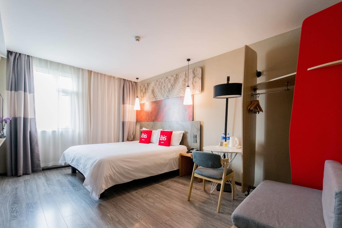 Une chambre d’hôtel avec un lit, un bureau, une chaise et un mur d’accent de couleur rouge.