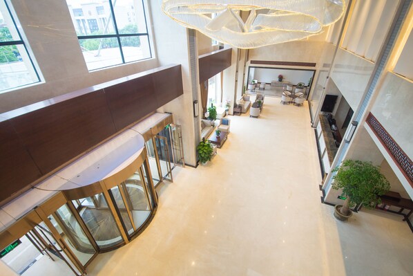 Eine geräumige Lobby mit hoher Decke, großen Fenstern und einer zentralen Sitzecke mit Sofas und einem Couchtisch.