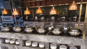 A buffet setup with multiple serving stations, stainless steel chafing dishes, and overhead copper lighting. - ibis Styles Nanjing Qilin Gate Hotel (Nanjing)