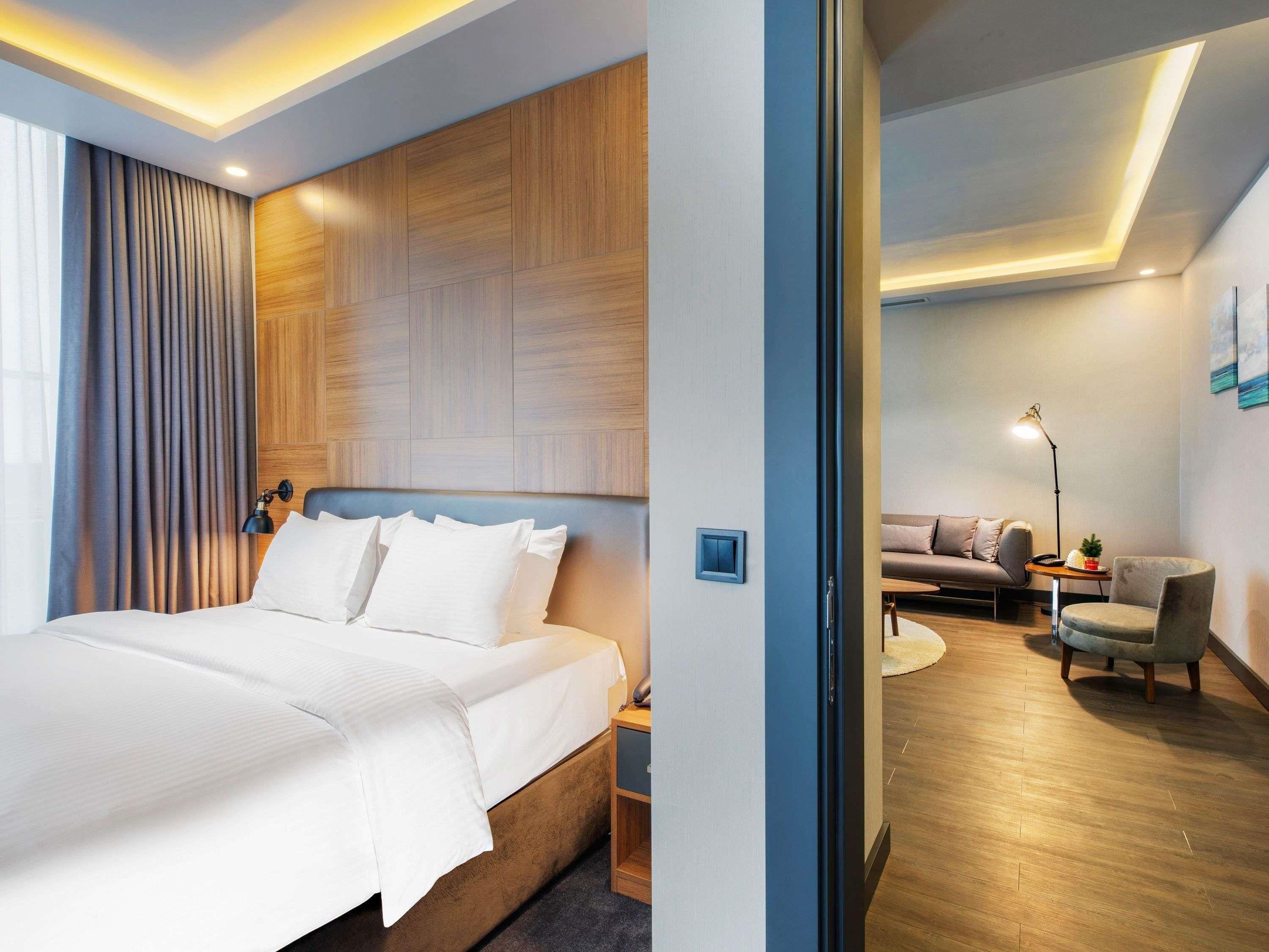 Habitación de hotel con una cama grande, cabecera de madera, escritorio, silla, sofá y lámpara.
