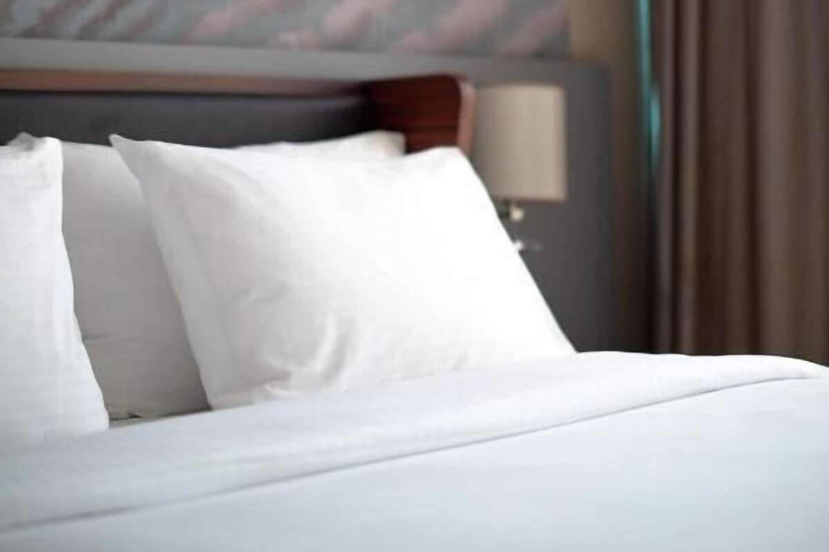 A neatly made bed with white bedding and pillows, a wooden headboard, and a wall with a marble-like pattern.