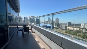 Un balcon offrant une vue sur le paysage urbain, avec des bâtiments modernes et une étendue d’eau.