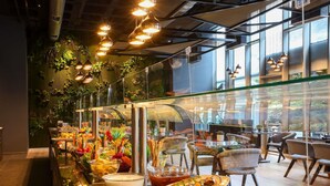 Een buffet met diverse gerechten, een zithoek met stoelen en een groot raam met uitzicht op groen.