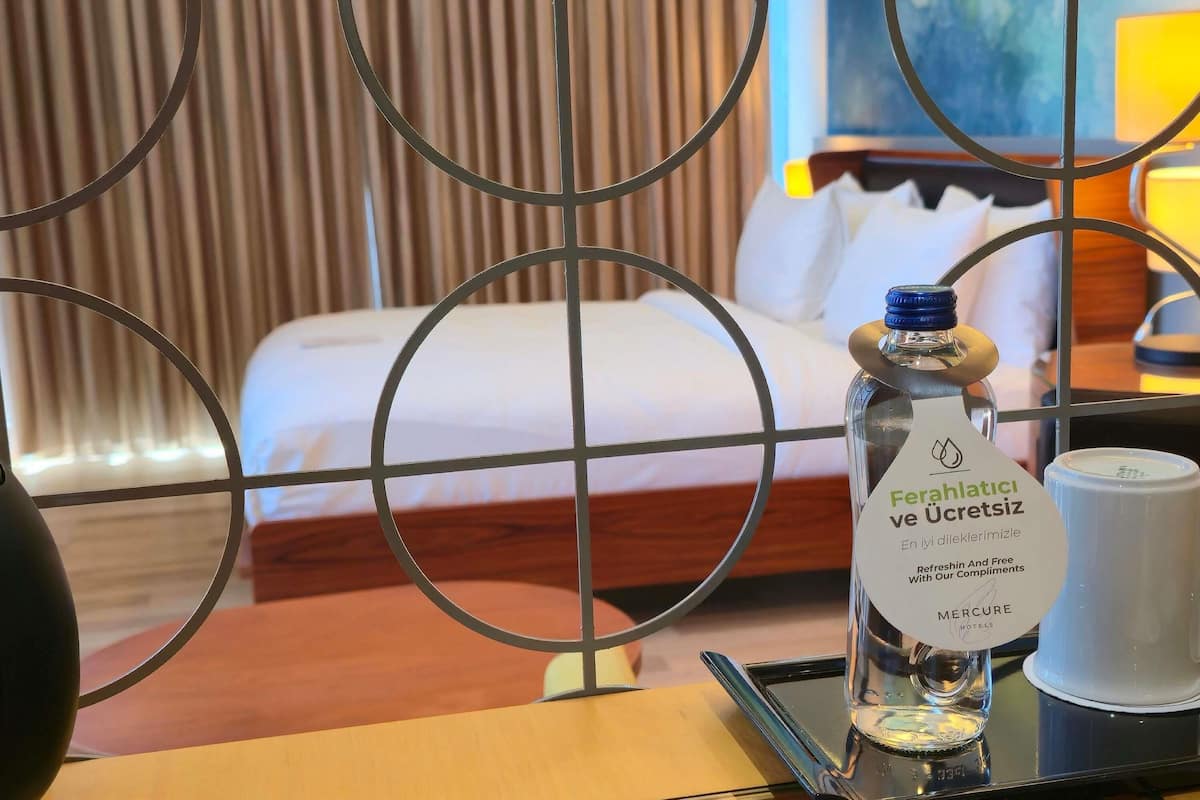 A hotel room with a bed, a bottle of water, and a tray with a cup.