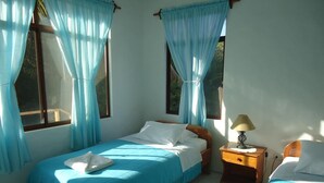 Un dormitorio con dos camas, una mesita de noche con lámpara y una ventana con cortinas.