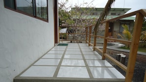 Una escalera conduce a un balcón con baranda de madera, con vistas a un jardín y un edificio al fondo.