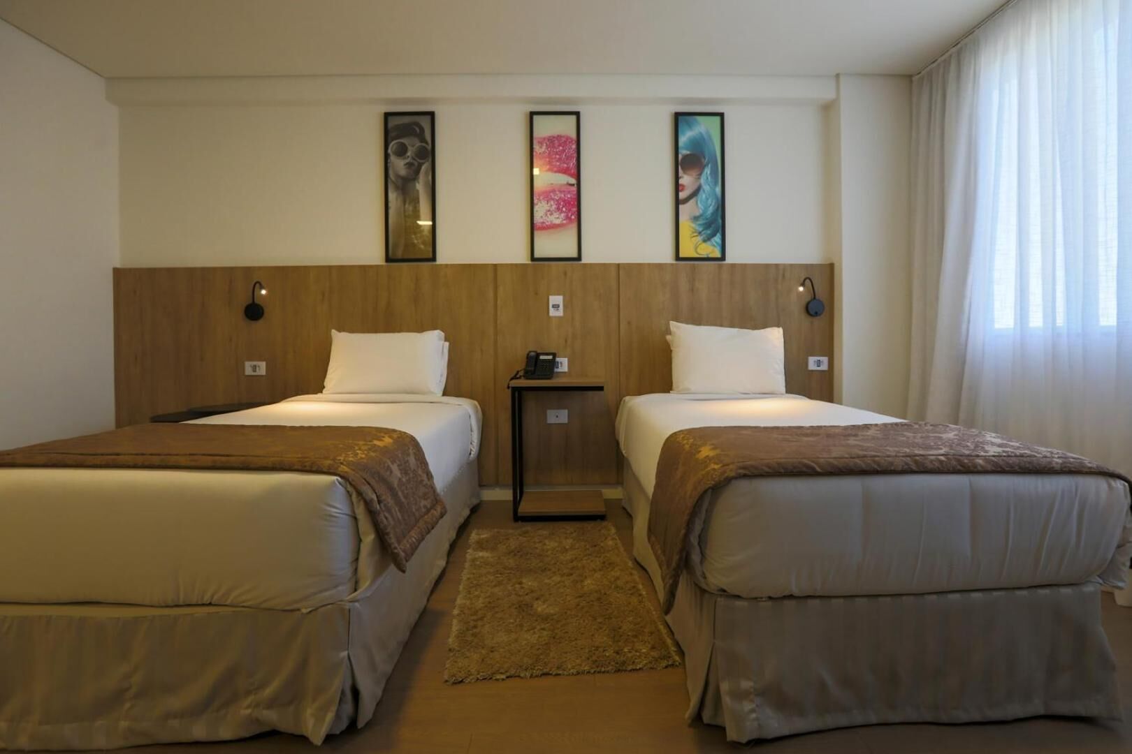 Habitación de hotel con dos camas, una mesita de noche con un teléfono y tres cuadros enmarcados en la pared.