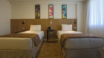 Habitación de hotel con dos camas, una mesita de noche con un teléfono y tres cuadros enmarcados en la pared.