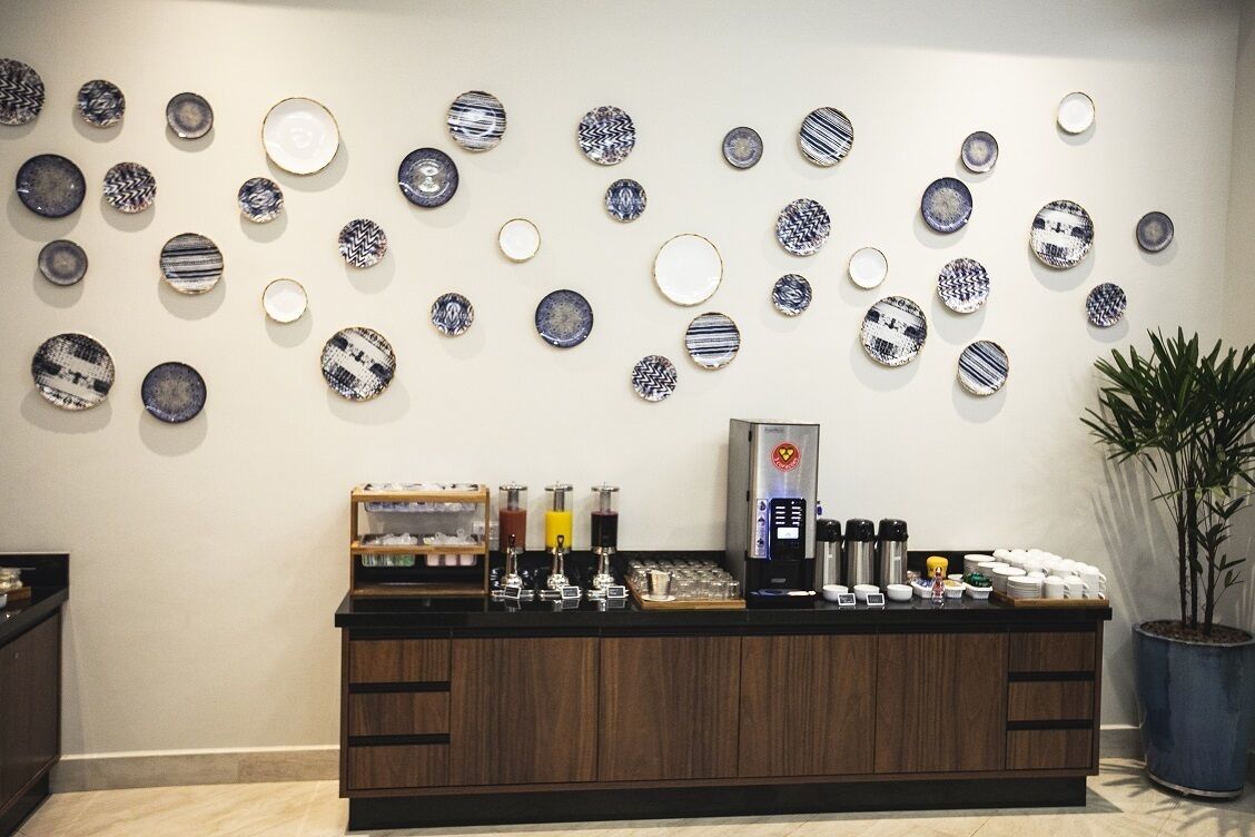 A reception area with a coffee station, wall-mounted plates, and a potted plant.
