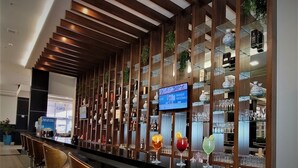 A modern bar area with wooden paneling, shelves with glassware, and a television screen displaying a sports channel. - Hotel Transamerica Maringá (Maringá)