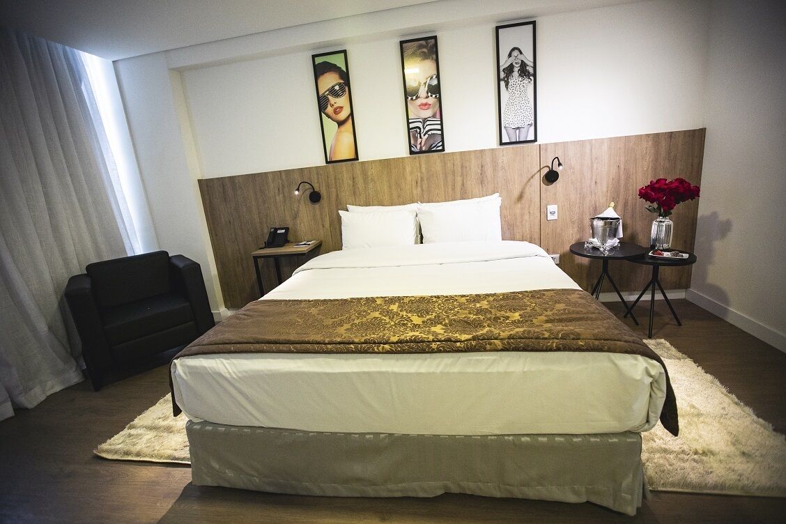 A hotel room with a large bed, a bedside table, a chair, and artwork on the wall.