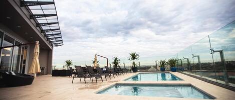 A rooftop pool area with lounge chairs and a glass balustrade.