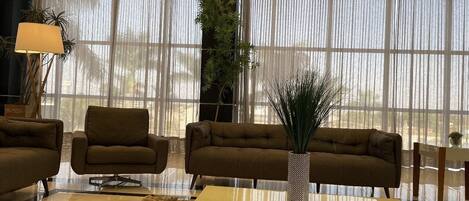 A modern living room with a sofa set, a coffee table, and a large window with sheer curtains.
