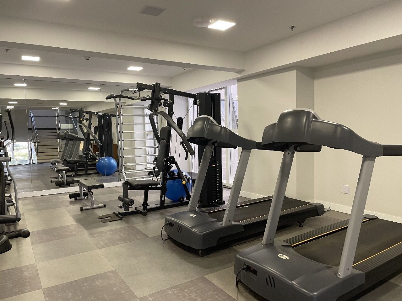 Academia com esteiras, máquinas de peso e um colchonete de exercício azul.