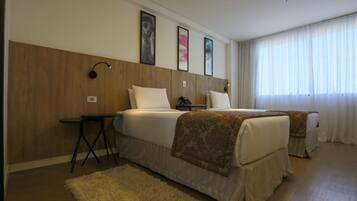 Habitación de hotel con dos camas, un escritorio y un ventanal grande con cortinas.