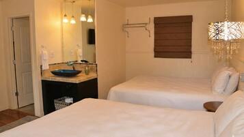 A hotel room with two beds, a bathroom with a sink and mirror, and a chandelier.
