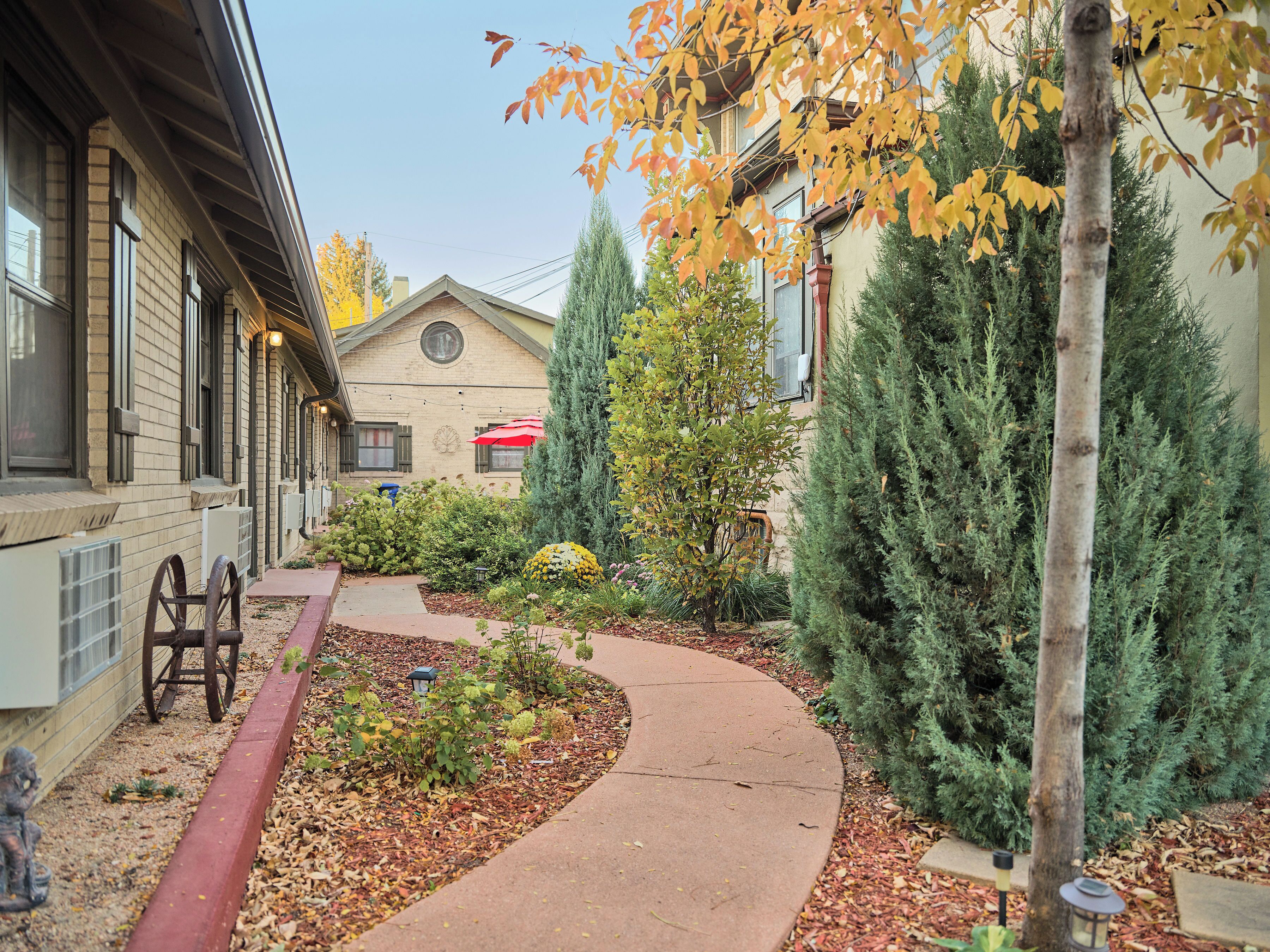 A building with a brick facade, a curved pathway, and various plants and trees.