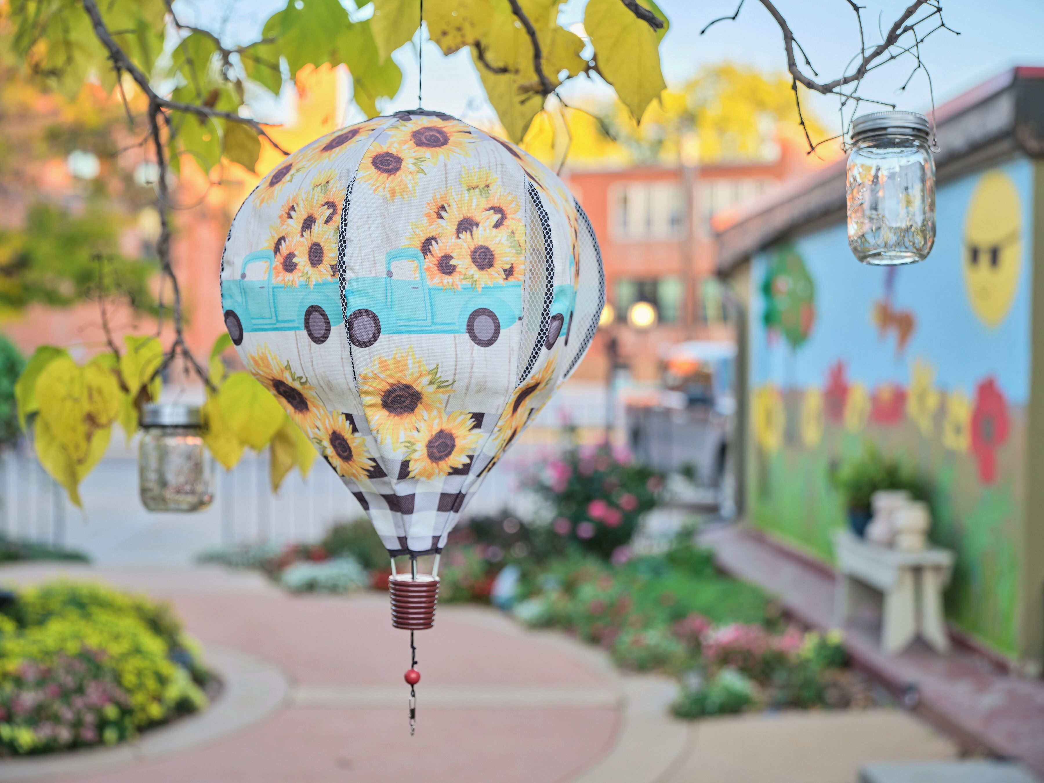 Un globo aerostático con diseños de girasoles, colgado de una rama de árbol.