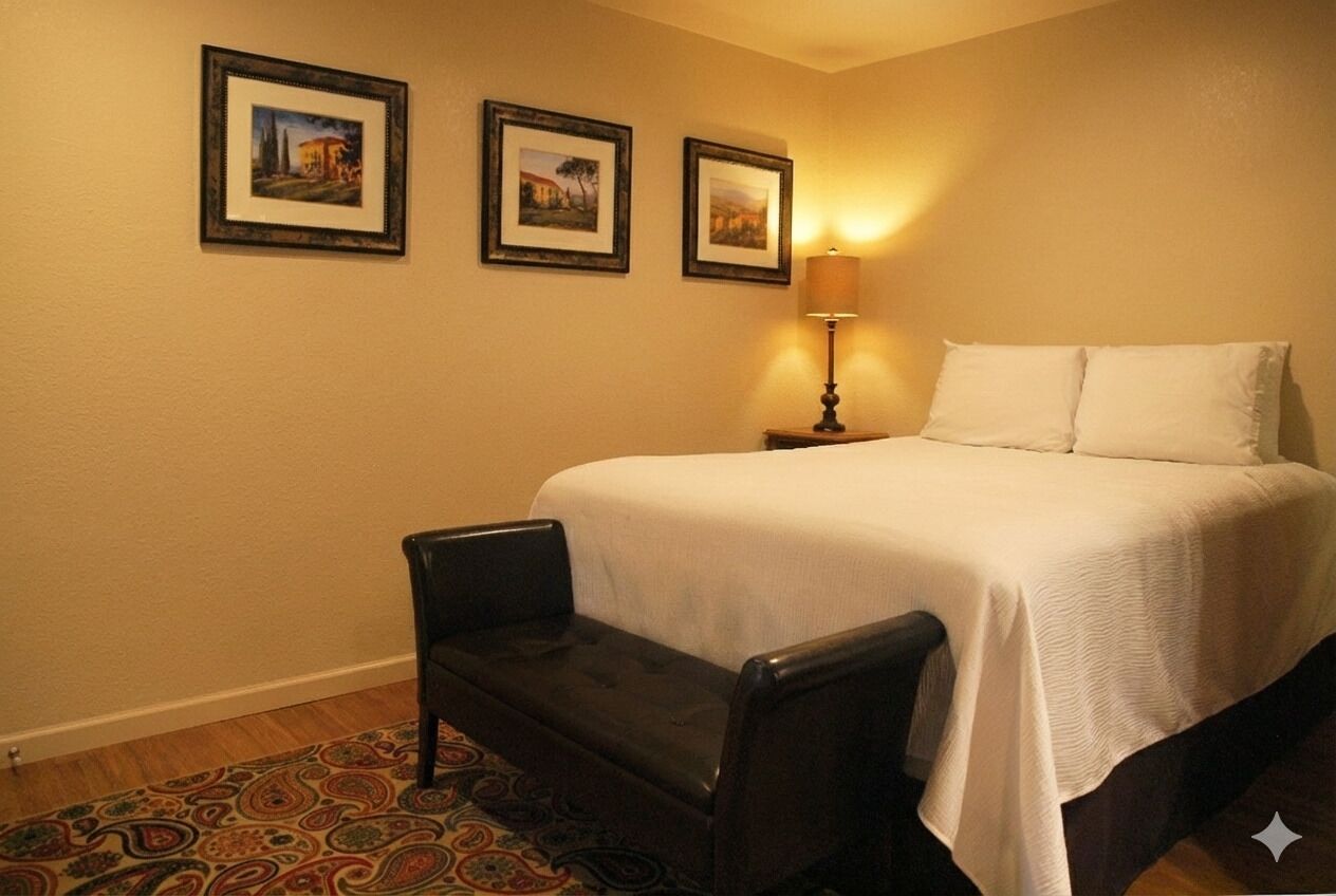 Une chambre d’hôtel avec un lit, une chaise, une lampe et trois tableaux encadrés accrochés au mur.
