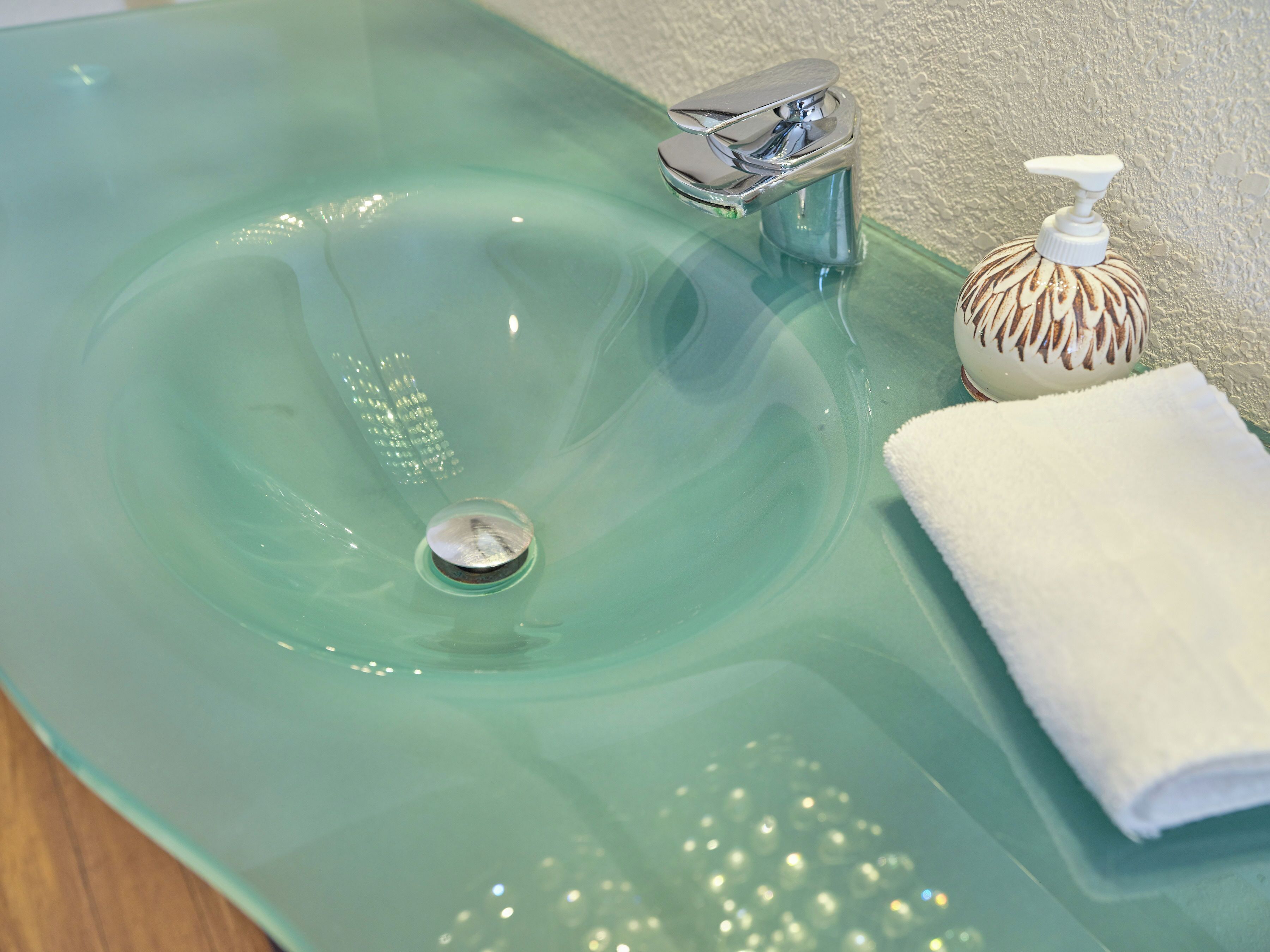 A clear glass sink with a chrome faucet and soap dispenser.