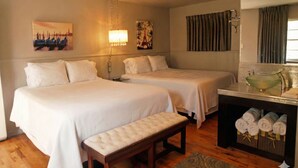 A hotel room with two beds, a bench, a vanity with a mirror, and a wall with artwork. - The Crest Motel in Colorful Colorado (Sterling)
