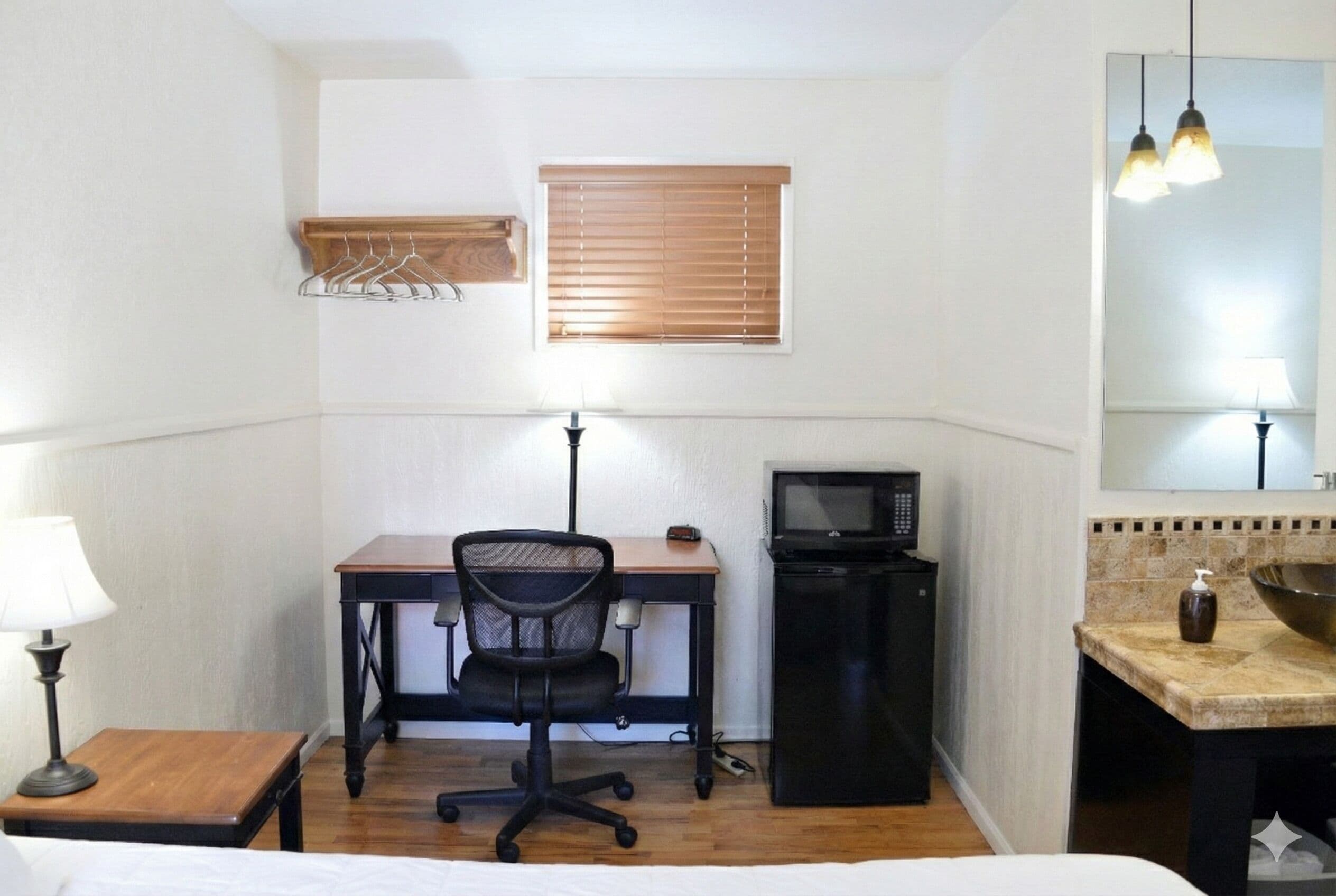 A small, compact room with a desk, chair, microwave, and a small sink.
