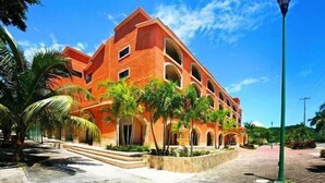Un edificio de varios pisos con fachada roja, ventanas en arco y un patio central con palmeras.