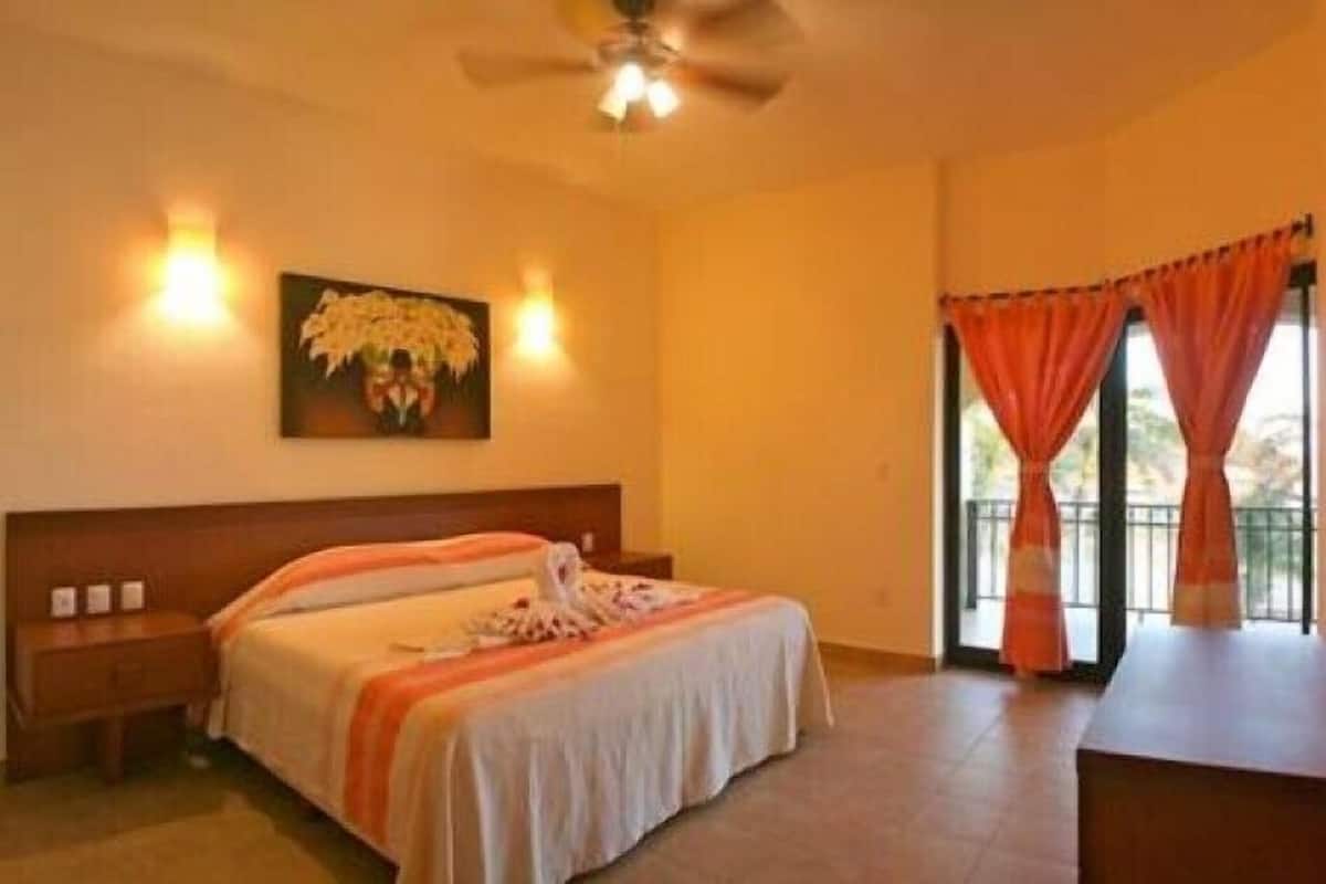 A hotel room with a bed, a nightstand, a ceiling fan, and a painting on the wall.