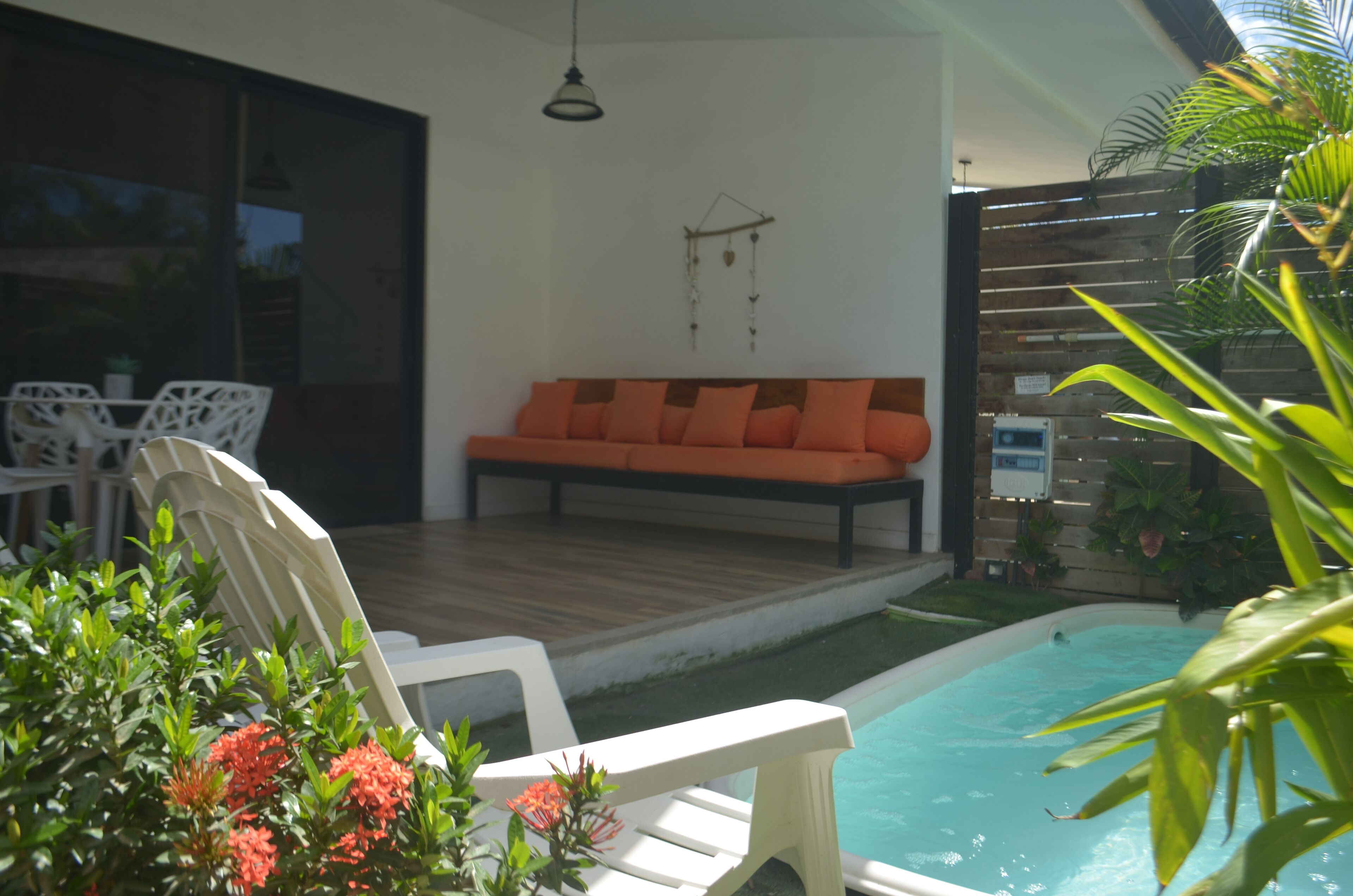 A modern outdoor seating area with a pool, white chairs, and orange cushions.