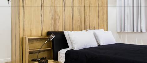 A modern bedroom with a wooden headboard, a black bedspread, white pillows, and a bedside lamp.