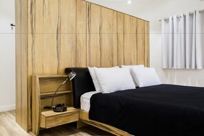 Une chambre à coucher moderne avec une tête de lit en bois, une couvre-lit noire, des oreillers blancs et une lampe de chevet.