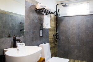 Un baño moderno con un lavamanos grande de color blanco, un grifo negro, un perchero con toallas, una zona de ducha y un espejo.