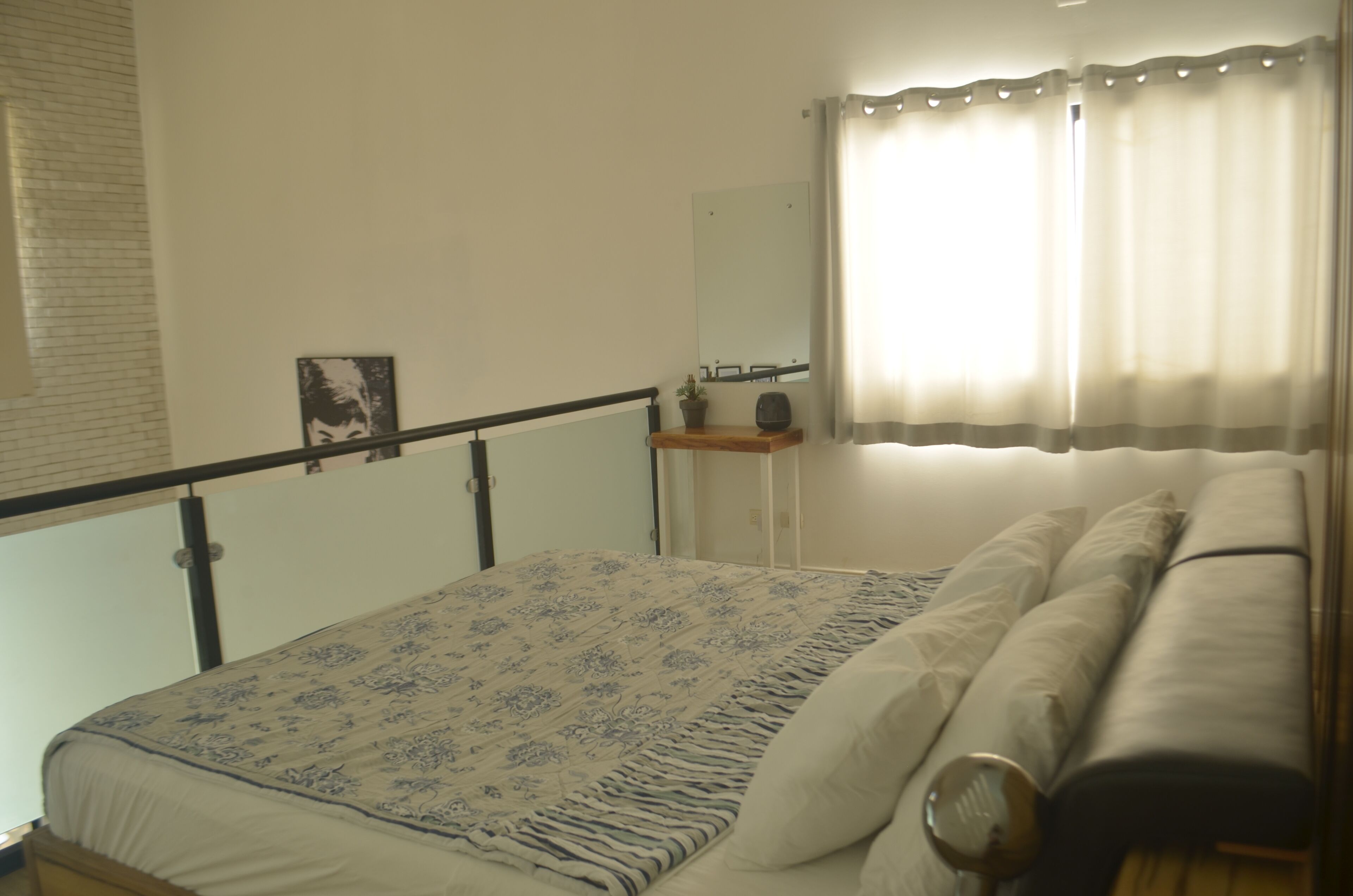 Une chambre à coucher avec un lit, une table de chevet, un miroir et une fenêtre avec des rideaux.