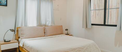 Un dormitorio con una cama de madera, una mesita de noche, una lámpara y un ventanal con cortinas.